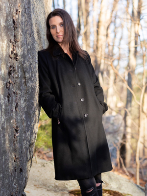 woman in black coat leaning against boulder